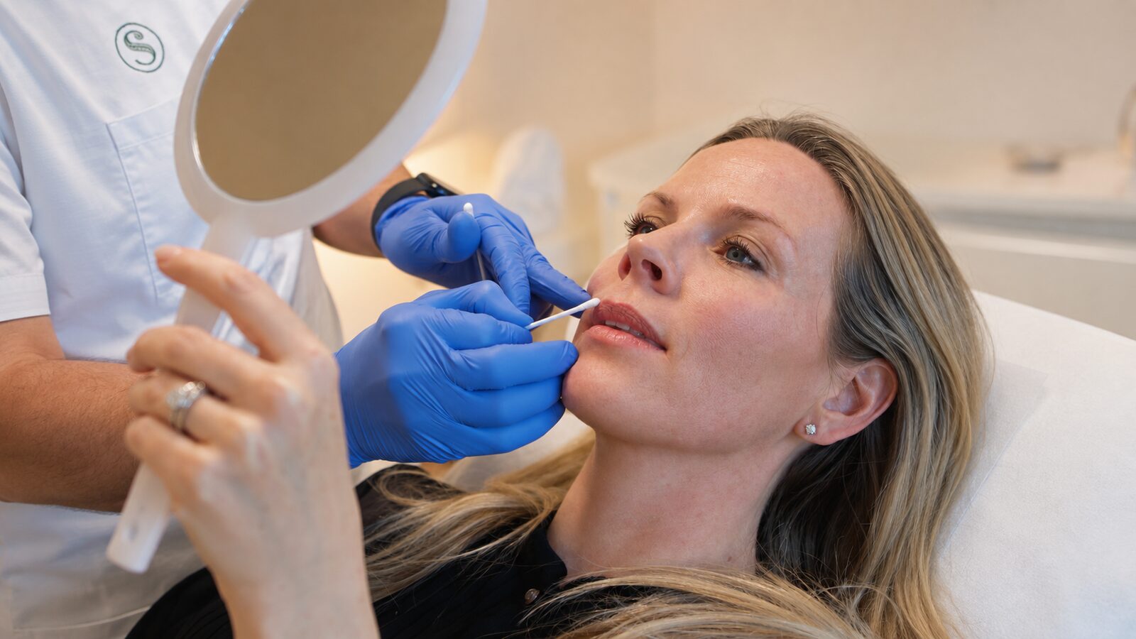 Ärztin führt bei Smoothline eine sanfte Lippenbehandlung durch, Patientin blickt in den Handspiegel